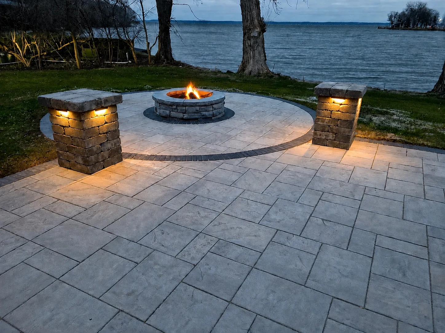 Natural fire burning in a circular stone firepit on an Earthscape lakeside paver patio