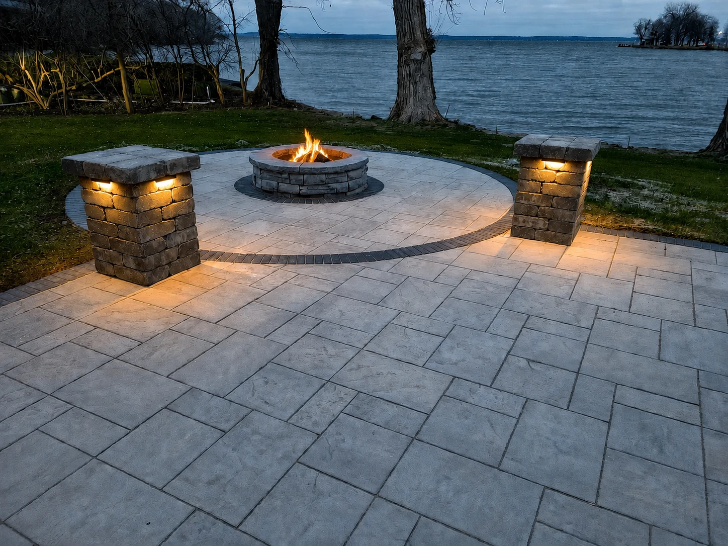 Earthscape lakeside stone patio with a fire burning in the central fire pit