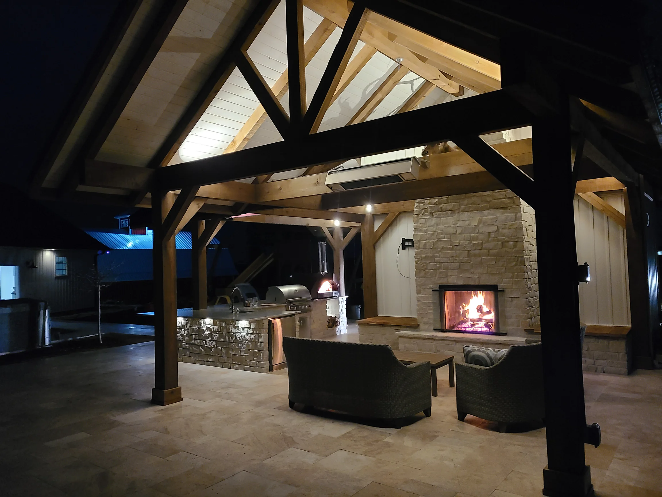 Timber pavilion with stone outdoor kitchen and fireplace illuminated at night