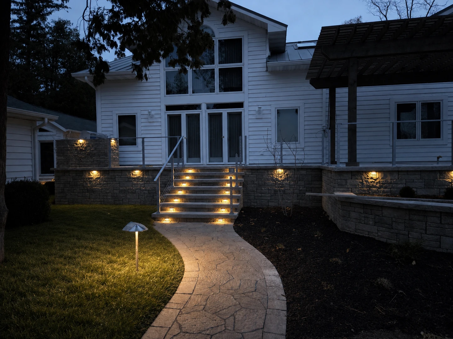 Finished curved paver walkway, lawn, mulched planting bed, and illuminated stone steps at dusk