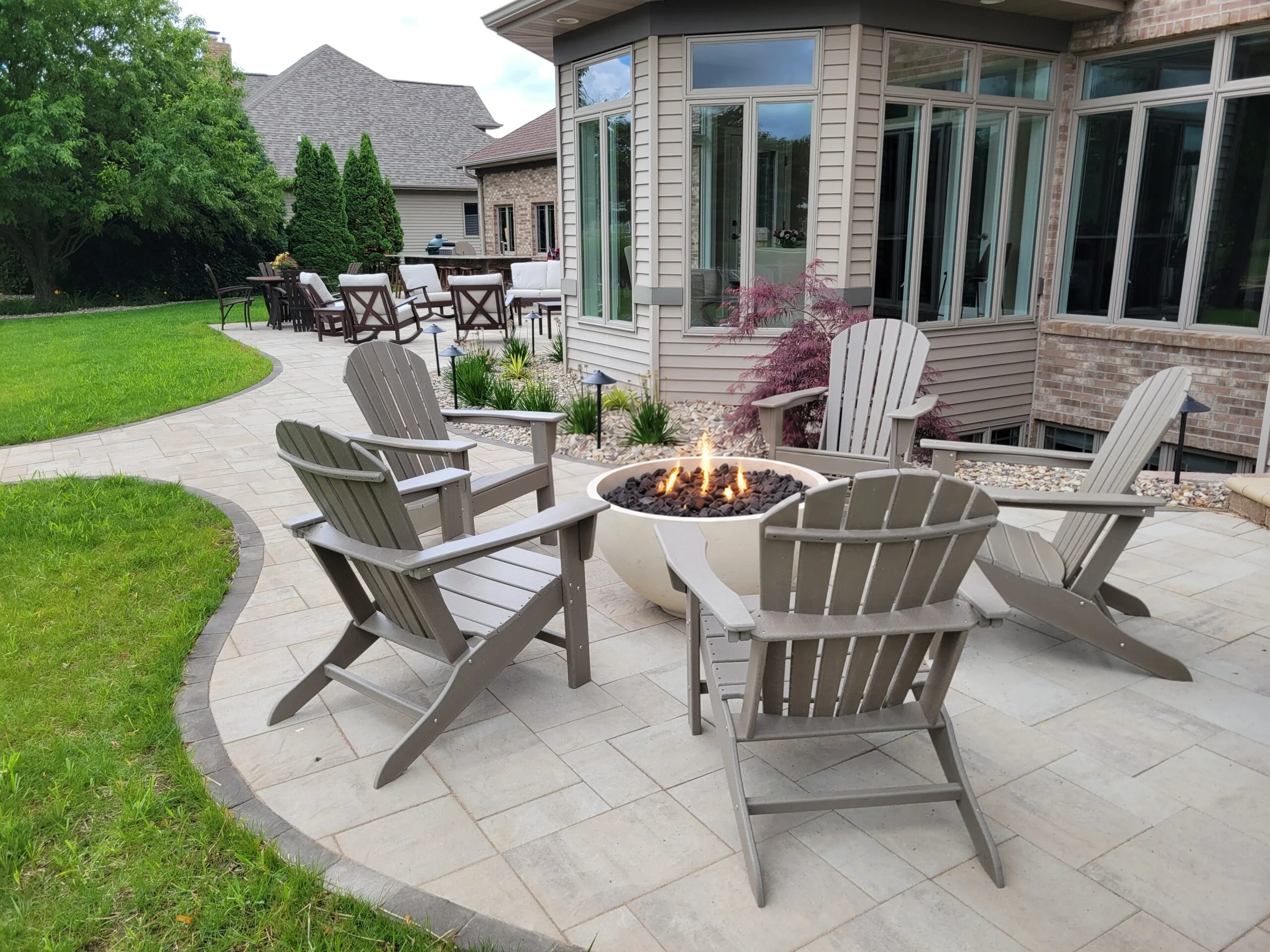 Earthscape curved paver patio with Adirondack seating around a lit gas fire bowl