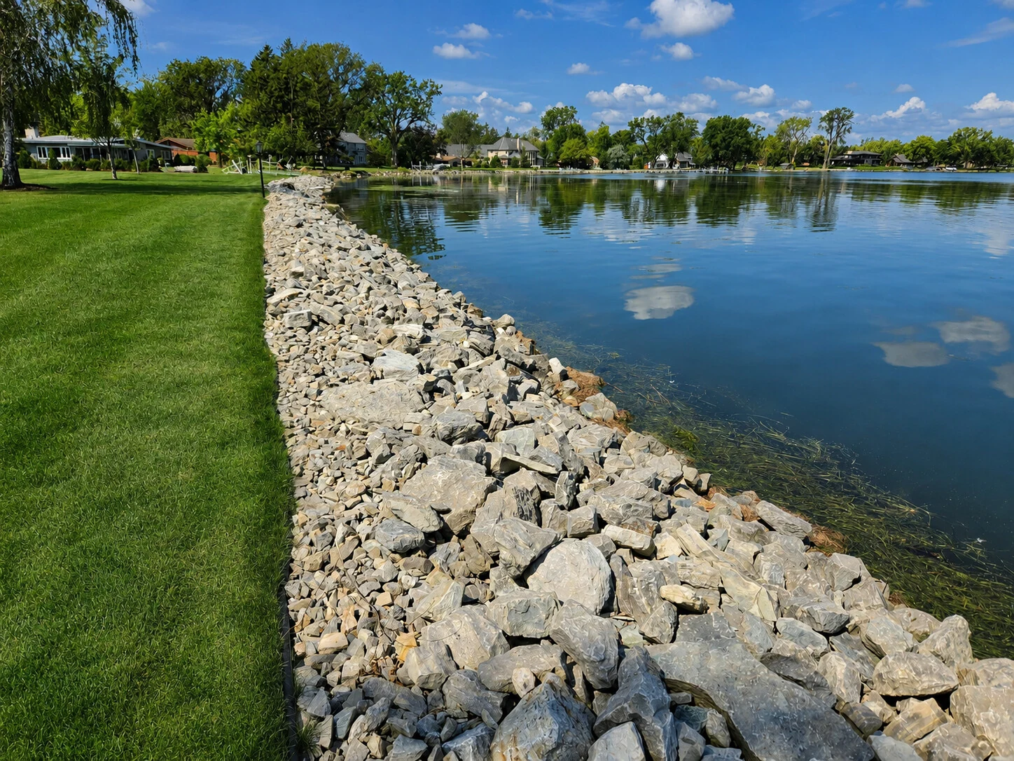 Riprap stone shoreline beside a green lawn and calm waterfront