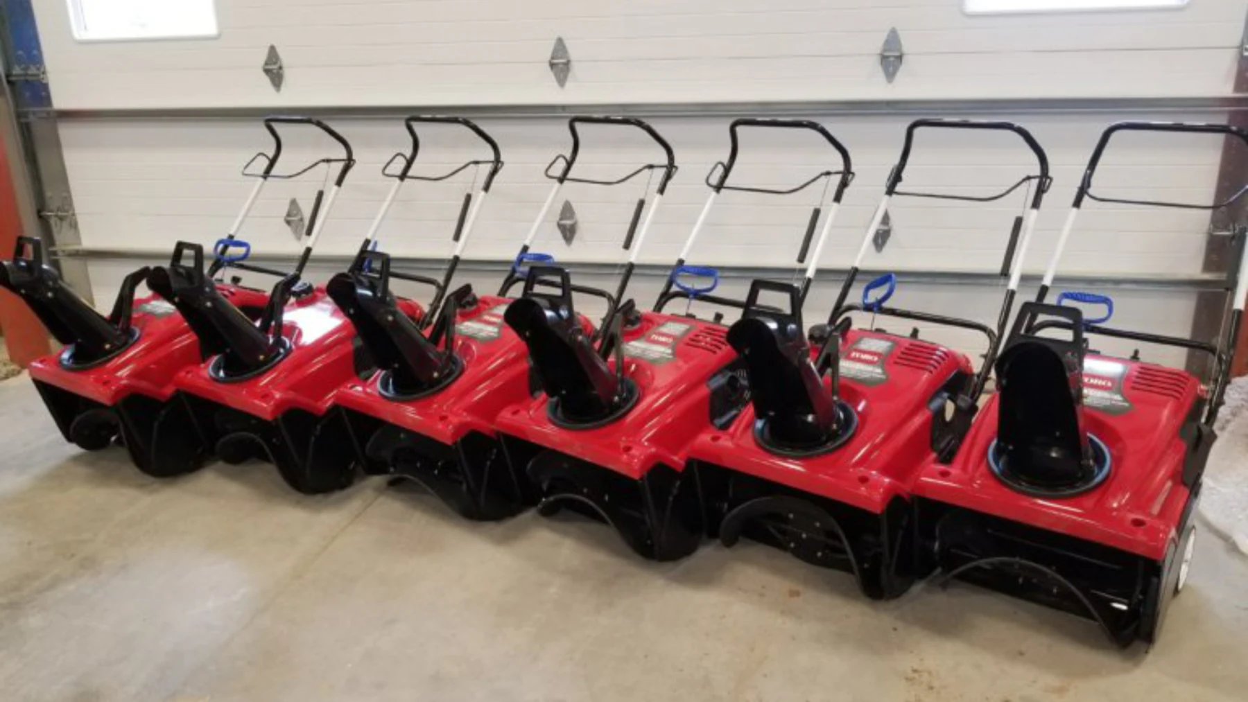A row of red snow blowers and shovels ready for sidewalk clearing