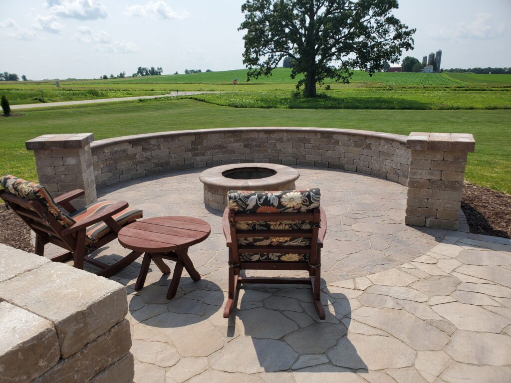 Stone fire pit and chairs enclosed by a curved masonry seat wall.