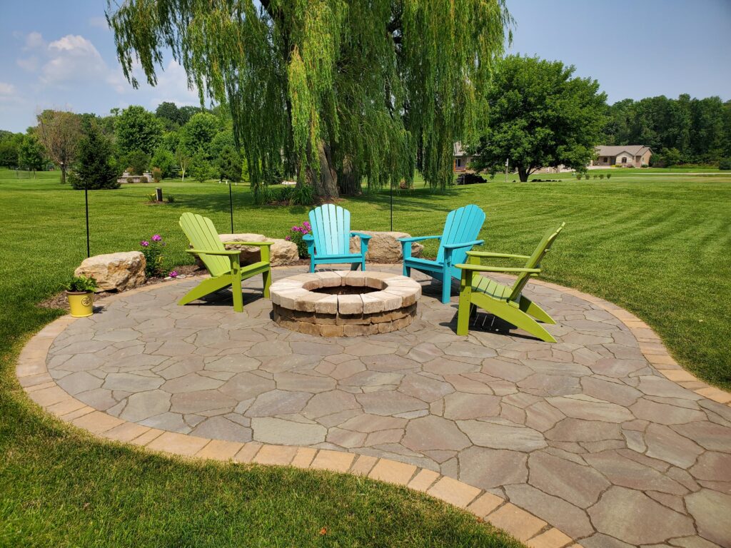 Bright Adirondack chairs surround a round fire pit on a lawn patio.