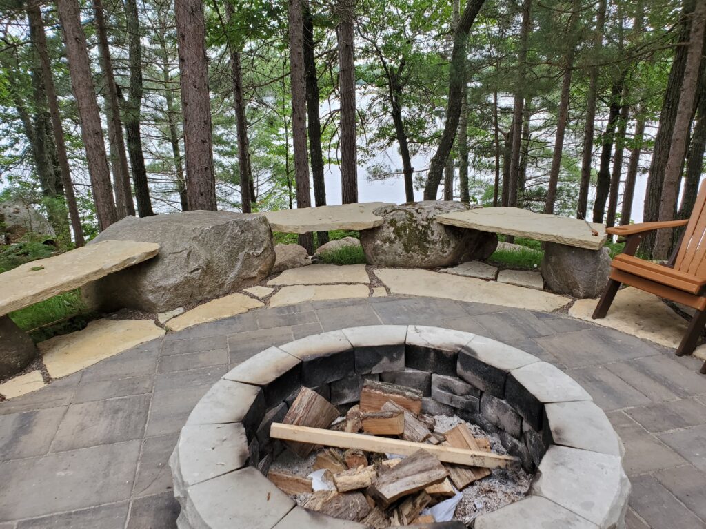 Rustic stone fire pit and boulder benches beneath mature trees.