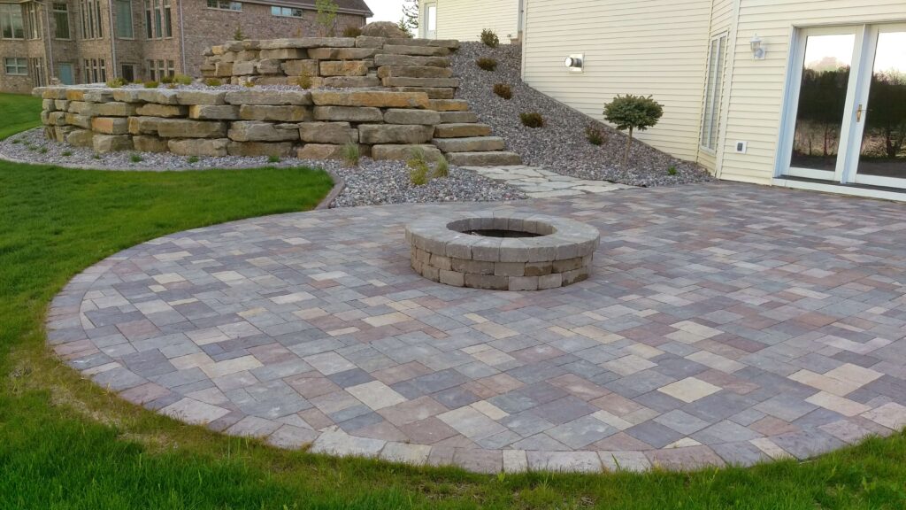 Stone fire ring built into a paver patio below terraced retaining walls.