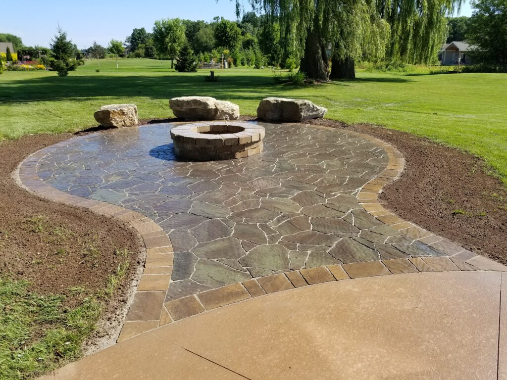 Round fire pit and boulder seating on a sweeping flagstone patio.