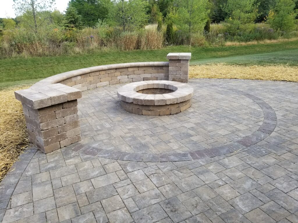 Stone fire pit centered on a paver patio with a curved seat wall.