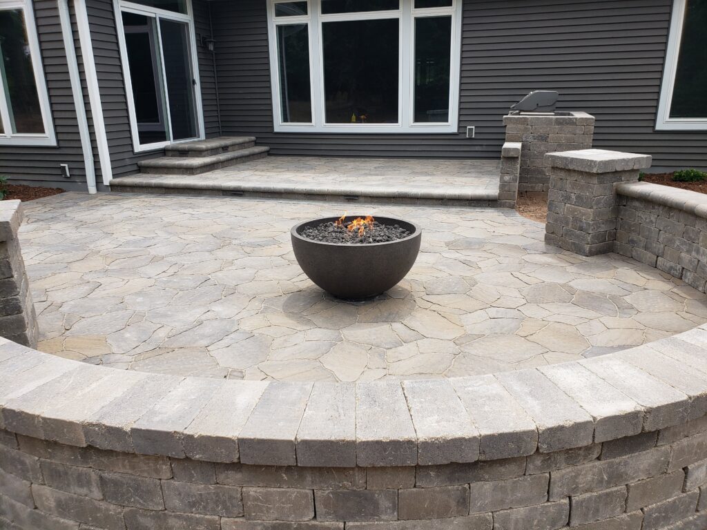 Lit metal fire bowl centered on a raised paver patio.