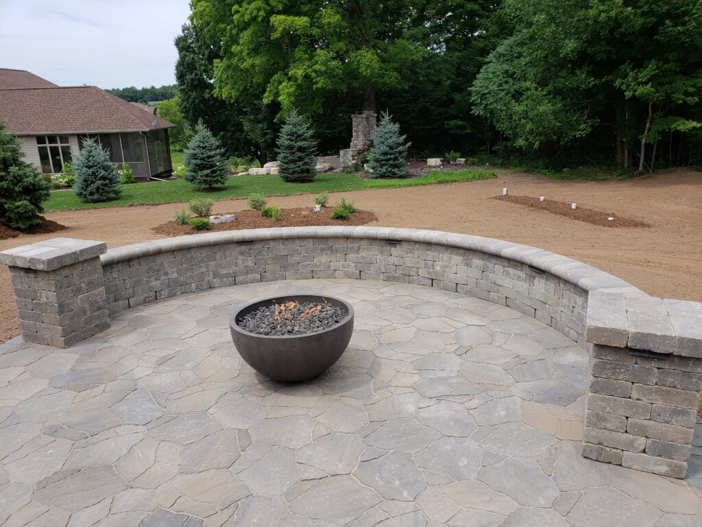 Round metal fire bowl within a curved paver seating area.