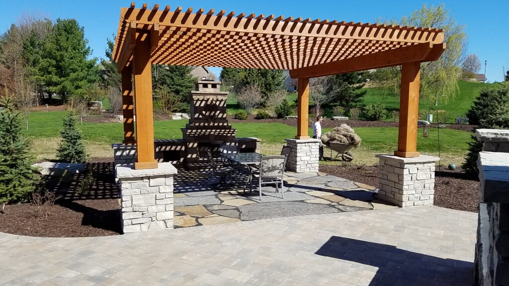Cedar pergola on stone columns shading a patio and outdoor fireplace.