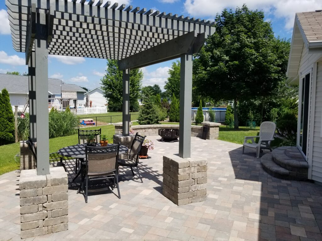 Gray pergola with stone columns shades dining furniture by the pool.