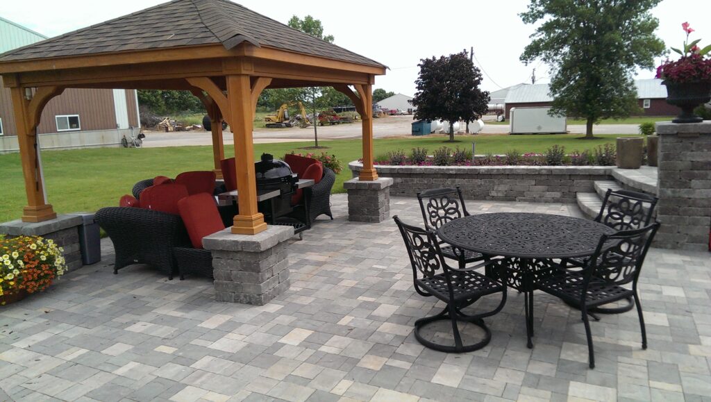 Cedar roofed pavilion shelters lounge seating on a paver patio.