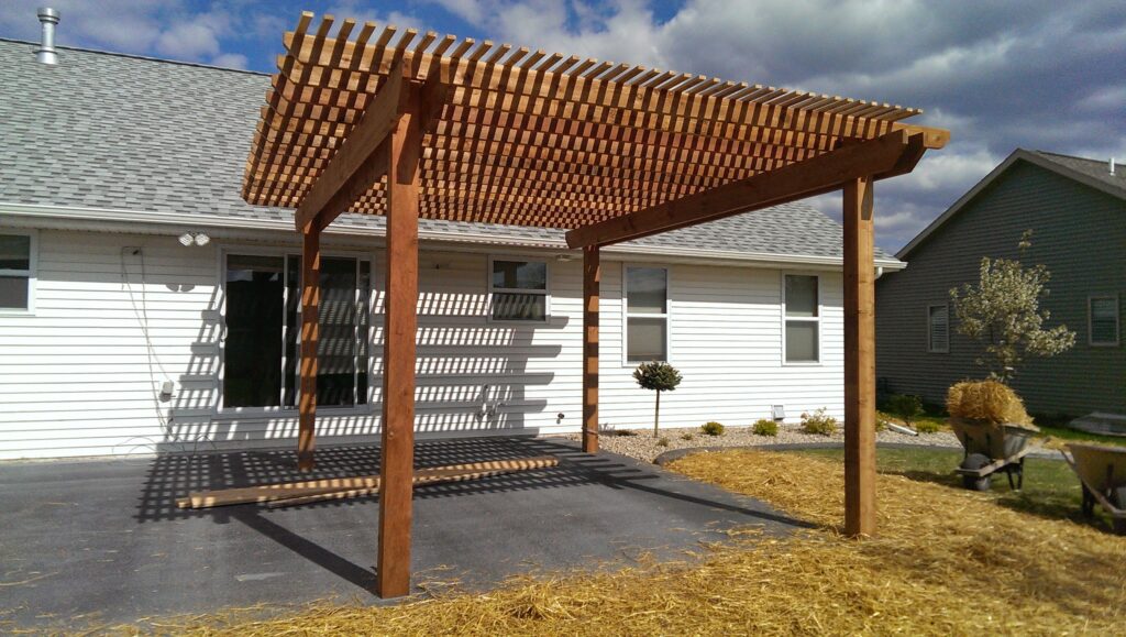 Compact cedar pergola extends shade beside a white garage.