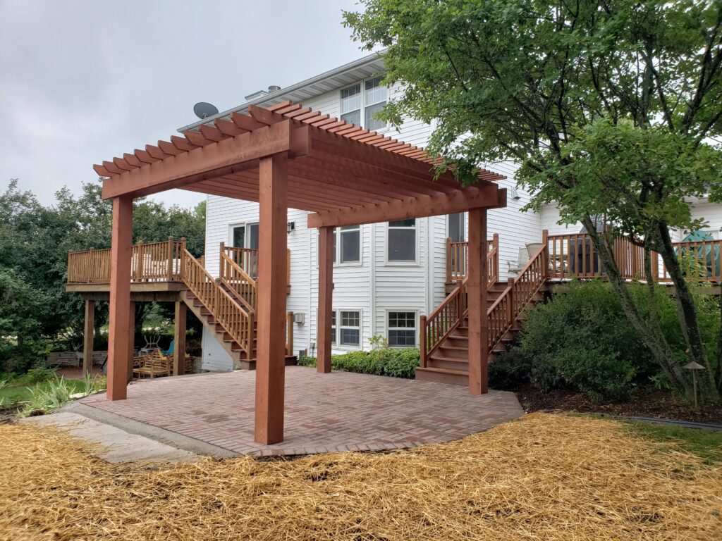 Freestanding cedar pergola over a brick patio beside a raised deck.