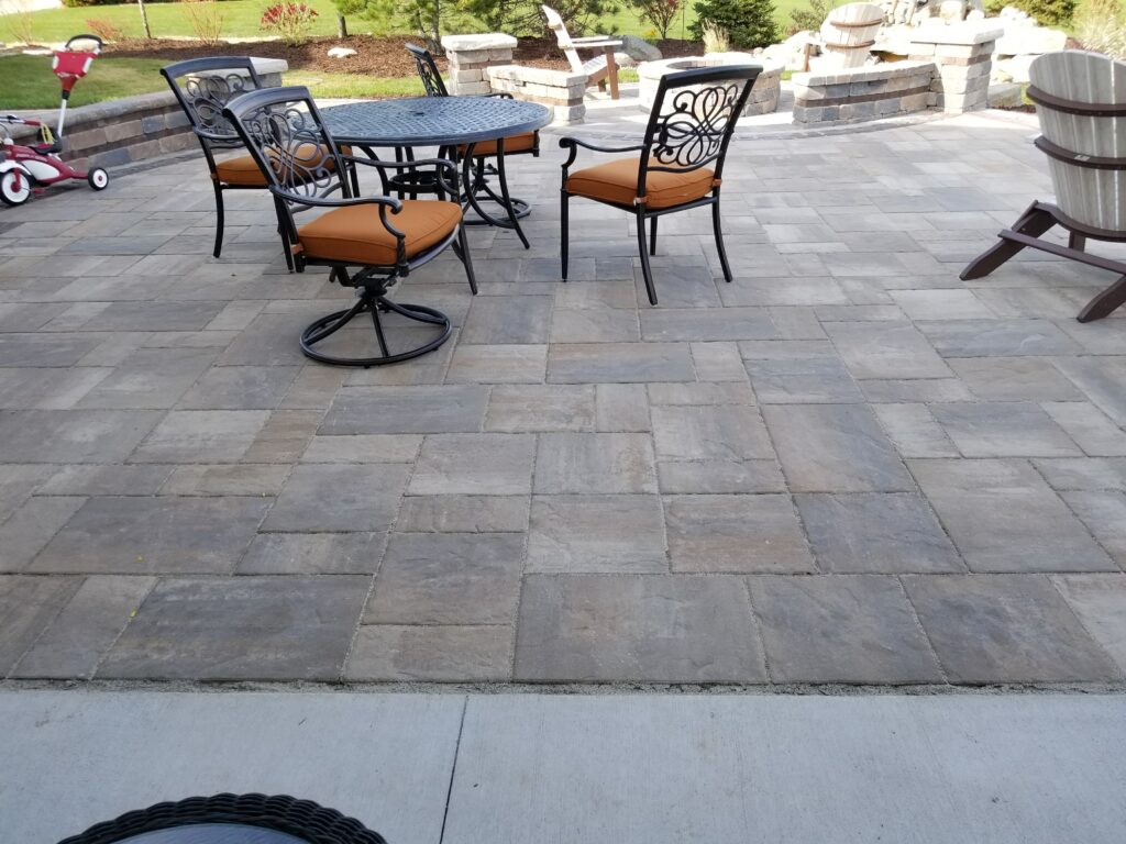 Gray paver patio furnished with a round dining table and chairs.