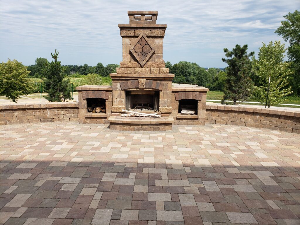Large paver patio centered on a stone outdoor fireplace and hearth.