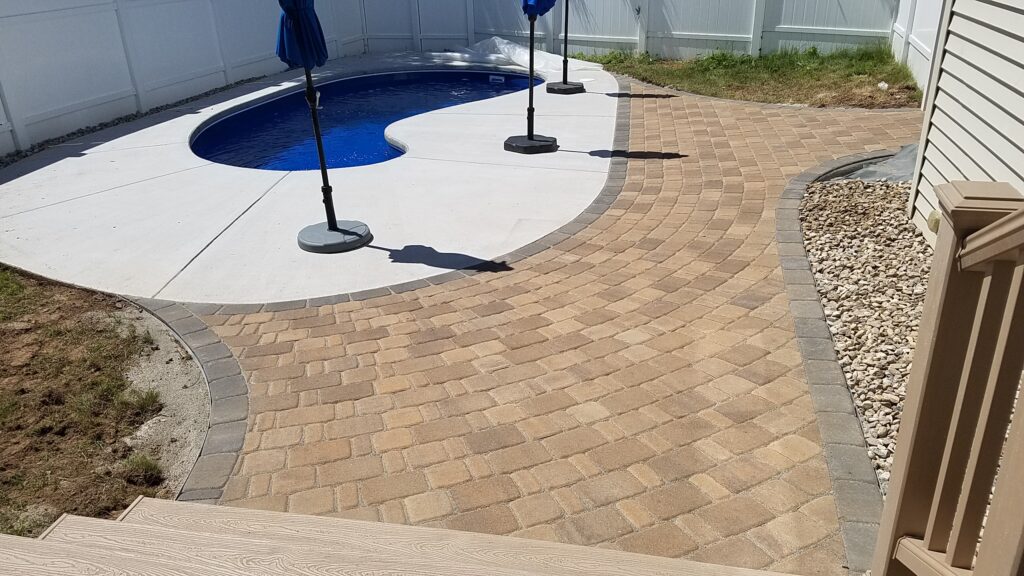 Curved tan paver patio surrounding an in-ground swimming pool.