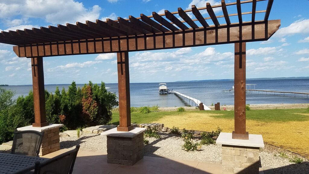 Cedar pergola frames a lake view from a paver patio.