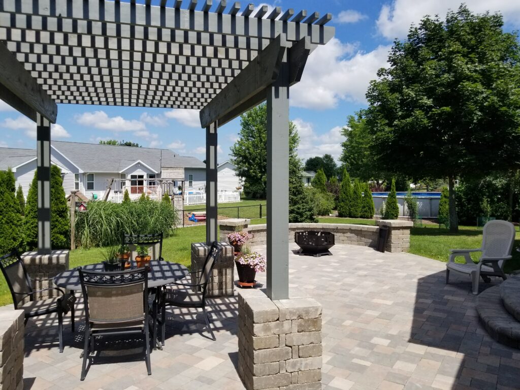 Gray pergola on stone columns shades an outdoor dining area.
