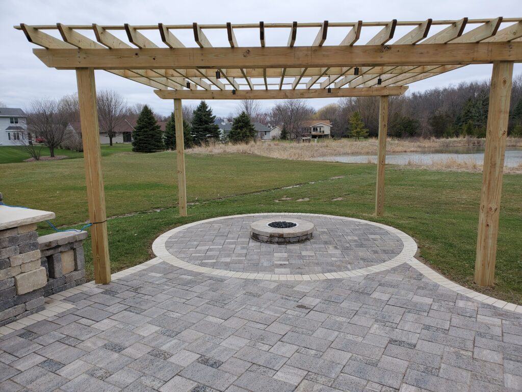 Natural cedar pergola spans a circular paver patio and fire ring.