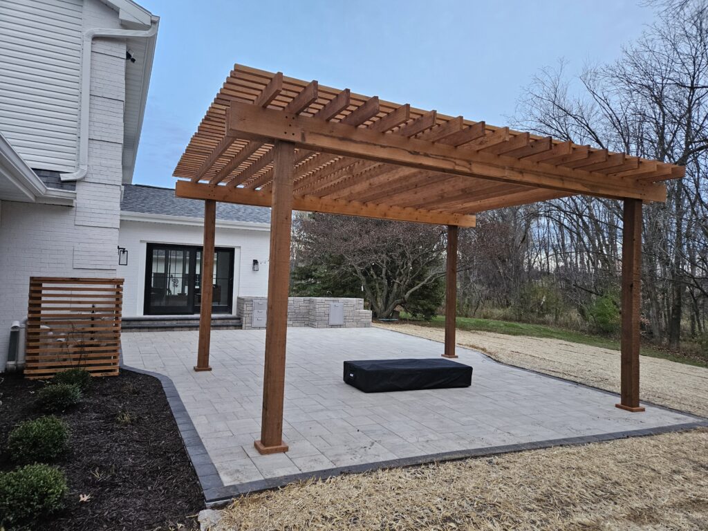 Freestanding cedar pergola shades a clean white-paver courtyard.