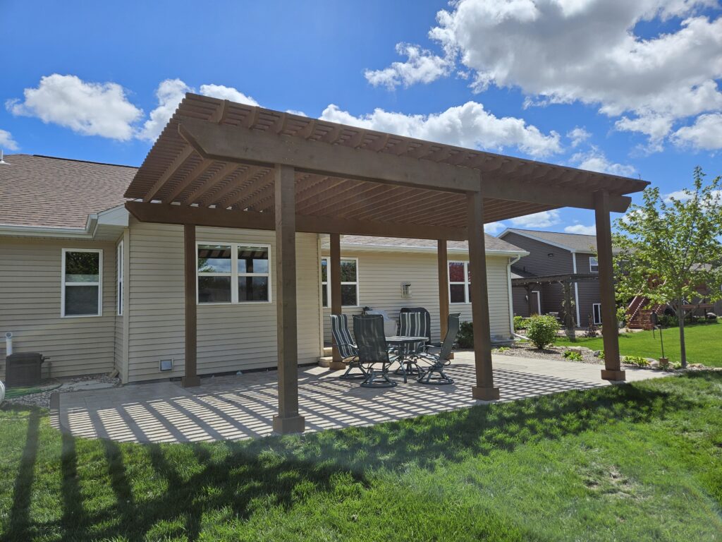 Flat-top cedar shade structure covers a dining patio behind the home.