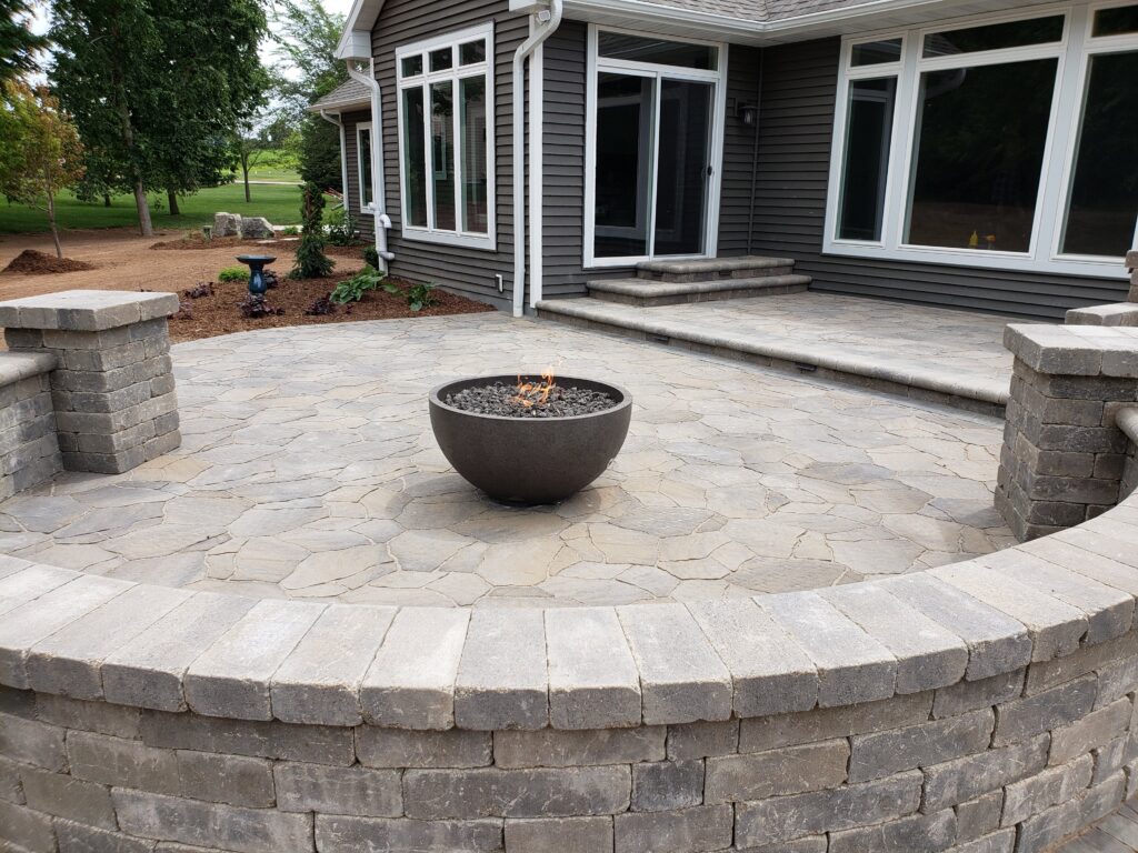 Metal fire bowl on a raised paver patio with curved seating wall.