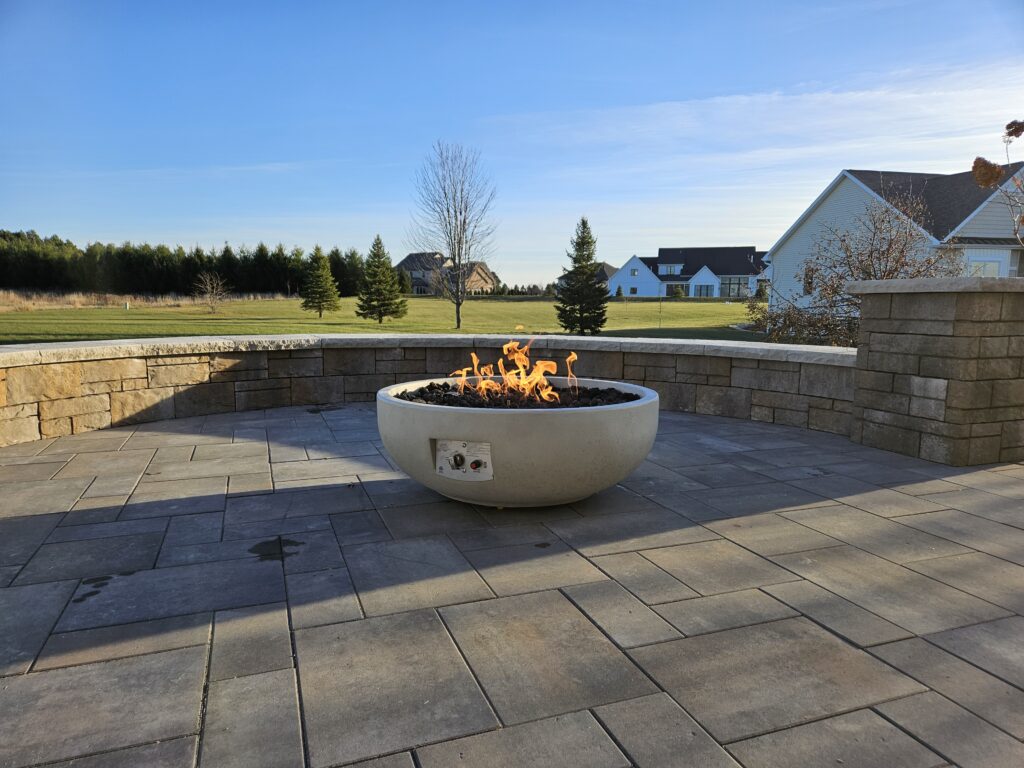 Flaming concrete fire bowl on a broad contemporary paver terrace.