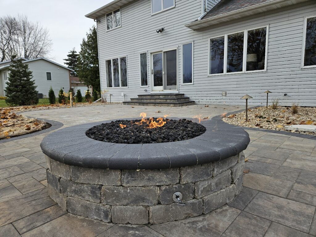 Circular gas fire pit built into a curved stone seat wall.