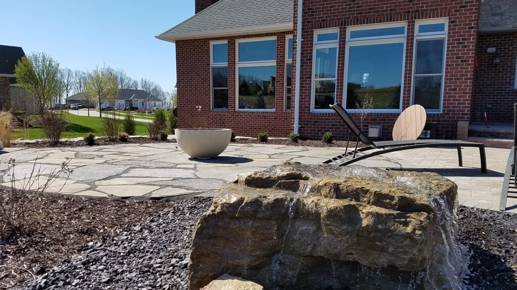 Curved paver terrace and landscaped beds along a brick home.