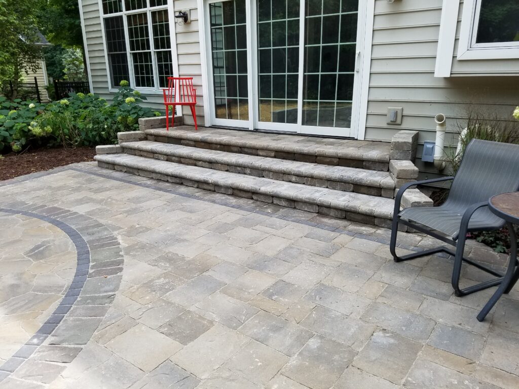 Broad curved paver steps with a decorative border beside the home.