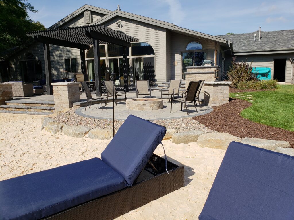 Furnished paver lounge and outdoor kitchen beneath a dark pergola.